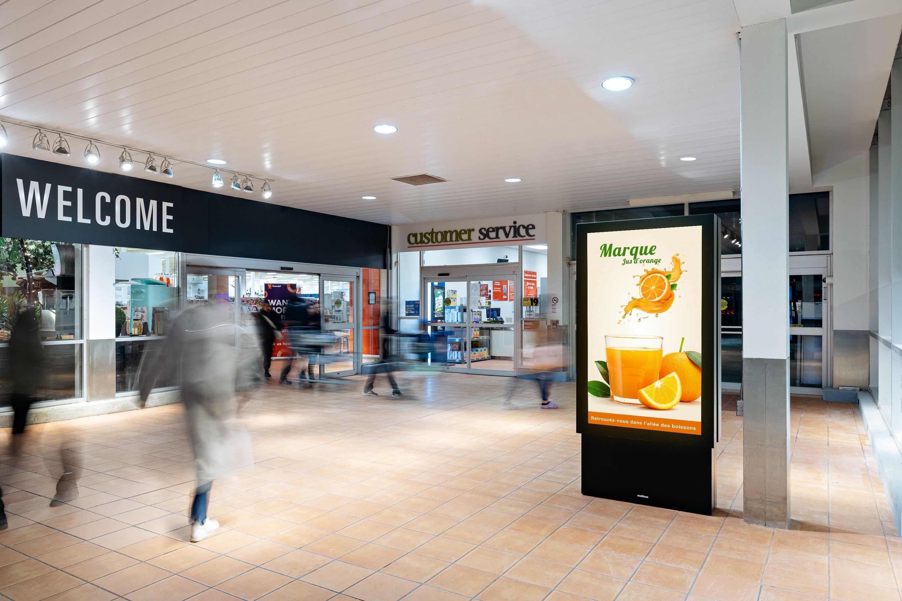 Un écran à l’entrée d’une épicerie avec une publicité pour du jus d’orange.